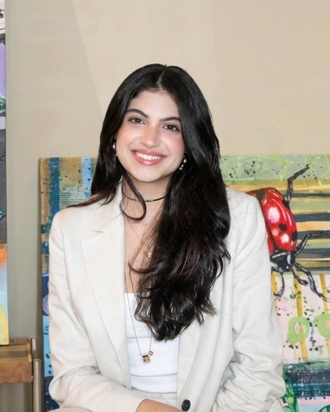 Luisa Barbalho, sorrindo, sentada no consultório, com quadros coloridos ao fundo
